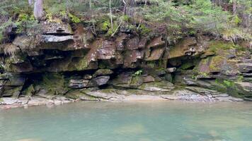 un' piccolo pittoresco lago con cristallo chiaro blu acqua con un' ripido roccioso riva nel il mezzo di un' pino foresta nel il mattina. un' Visualizza di il roccioso riva di un' foresta lago. laguna video