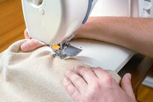 Male hands stitching white fabric on modern sewing machine. Close up view of sewing process. photo