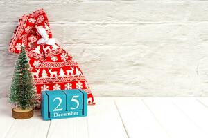 Red gift bag, Christmas tree and blue perpetual wooden calendar on white brick background. photo
