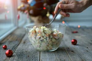 Homemade New Year is Olivier salad on a wooden background. A man's hand puts a traditional Russian Christmas salad with a spoon. photo