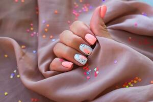 Women - a hand with a beautiful manicure holds a silk fabric on a background of sparkles. Pink trend, polishing the pattern on the nails with gel polish, shellac. Holiday photo