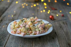 Homemade New Year is Olivier salad on a wooden background. Plate with a spoon of traditional Russian Christmas salad. photo