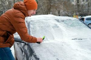 A man holds a brush in his hands and cleans the windows of the car from snow. The concept of transport, winter, weather, people and vehicles. photo