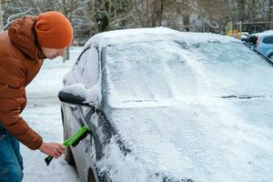 A man holds a brush in his hands and cleans the windows of the car from snow. The concept of transport, winter, weather, people and vehicles. photo