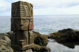 a wooden statue of a man standing on a rock near the ocean photo