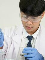 retrato asiático hombre estudiante científico o médico Mira mano participación reactivo mezcla laboratorio en Ciencias investigación laboratorio con prueba tubos de varios Talla en laboratorio química laboratorio blanco antecedentes foto