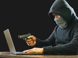 Portrait hacker spy man one person in black hoodie sitting on table looking computer laptop used login password attack security to data digital internet network system night dark background copy space photo