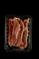 crudo carne en un el plastico envase en un negro antecedentes foto