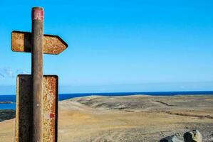 un oxidado firmar señalando a el Oceano en frente de un rocoso colina foto