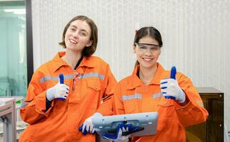 Female industrial engineer or technician worker in hard helmet and uniform using laptop checking on robotic arm machine. woman work hard in heavy technology invention industry photo