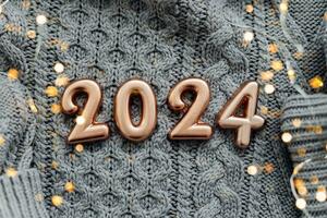 Christmas and New Year Greeting Card. Number 2024 on knitted gray background. Holiday lights bokeh background. Happy New Year 2024 Concept. photo