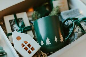 Christmas care package gift box. Paper box with cozy mug, candles, socks, candies and white ceramic house. Christmas and Holiday Gift Ideas photo