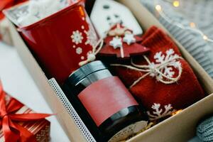 Christmas box with presents in red colors. Candle in dark jar, mug with marshmallow, white ceramic house, red socks and festive decoration. Top view photo