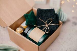 Christmas box with presents - candle in dark jar, chocolate candies, cozy grey socks and festive decoration. Personalized craft box for winter holidays photo