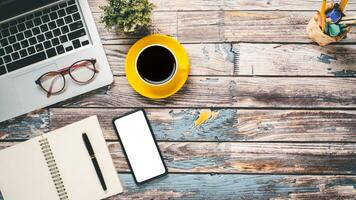 Wooden desk workplace with blank screen smartphone, laptop, eyeglass, pen, notebook and cup of coffee, Top viw flat lay with copy space. photo