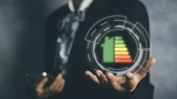 Person hand and house icon with energy efficiency scale image on black background, Concept of ecological and bio energetic house. Energy class. photo