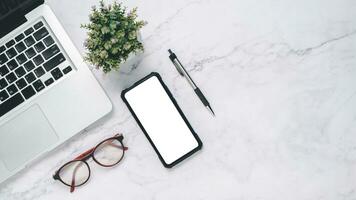 FLat lay, White office desk with laptop computer, blank screen smart phone, eyeglass and pen. Top view with copy space. photo