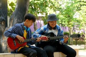 dos asiático Niños fueron teniendo divertido jugando clásico guitarra juntos durante su gratis hora a un colegio verano acampar a el parque. suave y selectivo enfocar. foto