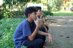 Two young Asian boys secretly sat down came to smoke in a hidden corner of the school. This is the behavior of finding a solution for teenagers who have problems in their lives by using substances. photo