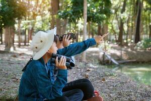 los niños asiáticos usan binoculares para observar las aves en un bosque comunitario. el concepto de aprendizaje de fuentes de aprendizaje fuera de la escuela. Centrarse en el primer hijo. foto