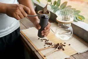 Asian man grinding coffee beans with grinder to easily drip black coffee at home, saving time and getting coffee that has a special aroma and taste. Soft and selective focus. photo