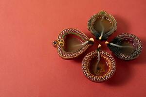 Happy Diwali and Kartika Deepam Festival Greetings - Clay diya oil lamps lit in celebration of Hindu festival of lights Diwali and Kartika Deepa on red background. photo