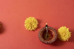 Happy Diwali and Kartika Deepam Festival Greetings - Colorful clay Deepam with yellow flowers on red background photo