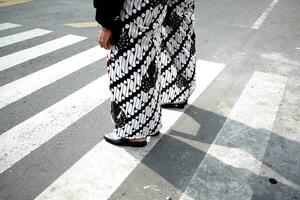 un persona en pie en un paso de peatones vistiendo negro y blanco pantalones foto
