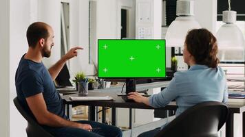 Corporate team using greenscreen on monitor while sitting at agency workstation, small business development. Man and woman colleagues looking at display showing isolated copyspace. video