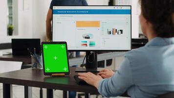agence employé à la recherche à tablette avec écran vert tandis que elle est dactylographie information sur ordinateur, vérification maquette modèle sur moderne gadget. femme travail sur affaires avec chromakey dans bureau. video