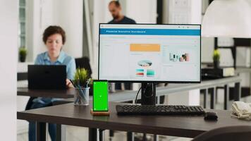 Persons conducting business tasks at agency workspace with cellphone displaying greenscreen at empty desk. Isolated copyspace mockup layout appears on workstation with mobile device. video