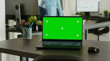 Wireless pc with greenscreen at empty desk in creative agency workplace, laptop showing blank copyspace on display. People working on startup business, workstation with mockup template. video