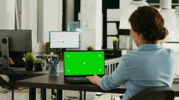 Specialist using laptop with greenscreen to solve business tasks and operations in office, looking at chromakey display in coworking space. Woman working on wireless pc with copyspace. video