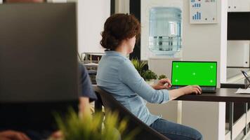 Office worker checks greenscreen on laptop, working in small business agency. Woman looking at screen showing isolated mockup template with chromakey copyspace, coworking space. video