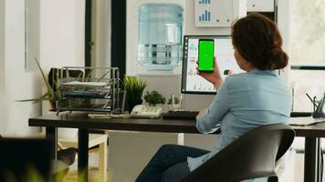 anställd innehar smartphone i hand och som visar grönskärm visa i små företag kontor. ung kvinna ser på mobil enhet med isolerat attrapp copy på skärm layout. video