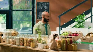 cliente entrata Locale drogheria memorizzare per acquistare biologico frutta e la verdura, guardare a pasta e cereali immagazzinato nel sostenibile non inquinante bicchiere barattoli. mezzo orientale uomo pubblicità salutare mangiare. video