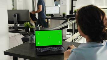 Employee uses greenscreen layout on laptop, working on business operations and marketing tasks. Specialist examining pc with isolated copyspace mockup template in open office. Handheld shot. video
