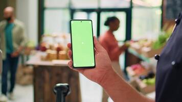 eigenaar toepassingen groene scherm Aan smartphone, tonen geïsoleerd Chroma sleutel sjabloon Aan apparaat in lokaal biologisch nul verspilling eco markt. jong verkoper presenteert copyspace mockup Scherm. video