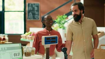 mensen buying biologisch produceren Bij nul verspilling op te slaan register, verkoper gebruik makend van elektronisch schaal Bij biologisch markt uitchecken bureau. handelaar weging fruit en groenten, gezond aan het eten. statief schot. video