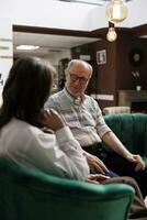 Retired senior husband and wife seated on comfortable sofas in lounge area planning their vacation activities. Happy elderly couple discussing holiday itinerary at exclusive hotel reception. photo