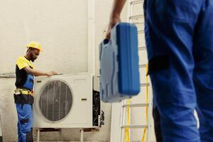 Engineer arriving on location to help apprentice mend busted electric coils in damaged external air conditioner. Technicians comissioned to prevent internal parts breakdowns, ensuring timely repair photo