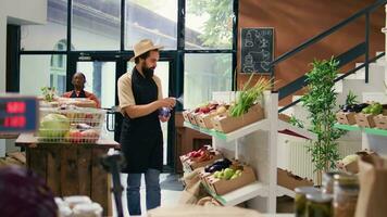 mercante spruzzatura maturo produrre per conserva fresco aroma, zero rifiuto eco memorizzare venditore. attività commerciale proprietario con cappello e grembiule assunzione cura di frutta e verdure immagazzinato nel casse, biologico negozio. video