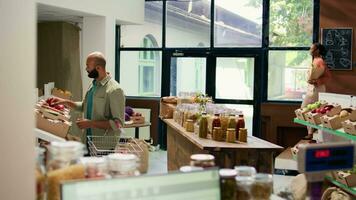 klant op zoek Bij vers groenten Aan schappen Bij lokaal nul verspilling eco op te slaan, kiezen naar kopen van eigen bodem produceren voor duurzame levensstijl en veganistisch voeding. Mens aan het doen boodschappen doen Bij ecologisch winkel. video