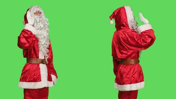 Person in santa claus suit wave hello on camera, acting joyful and confident over greenscreen backdrop. Festive seasonal character greeting people or saying goodbye, isolated template. photo