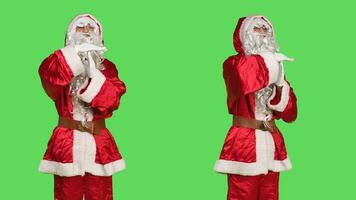 Saint nick cosplay shows timeout symbol, posing in festive seasonal costume over greenscreen backdrop. Young man representing father christmas asking for a break, does pause sign. photo
