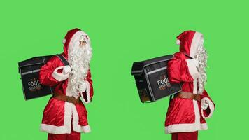 Santa claus carries delivery bag over greenscreen backdrop, working on delivering fast food orders with festive xmas costume. Joyful person in christmas holiday character, studio shot. photo