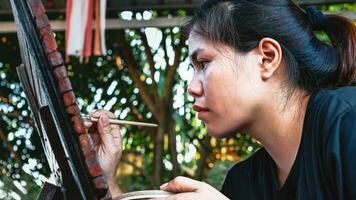 Asian woman painter creating art use a paintbrush to draw lettering designs on a wooden coffee shop sign. outdoor activities, People doing activities. photo