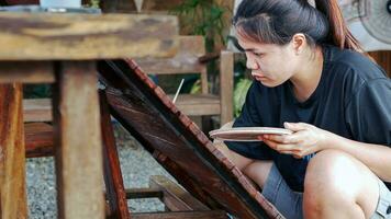 asiático mujer pintor creando Arte utilizar un Cepillo de pintura a dibujar letras diseños en un de madera café tienda firmar.al aire libre actividades, personas haciendo actividades. foto