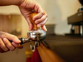 Hand of a barista holding a portafilter and a coffee tamper making an espresso coffee. Barista presses ground coffee using a tamper in a coffee shop photo