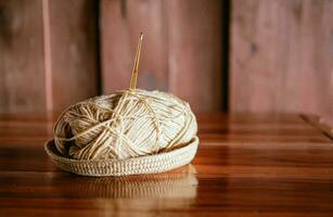 A yarn with a knitting needle stuck in it lies on a wooden table,Hobby crafts with yarn,hand made. photo